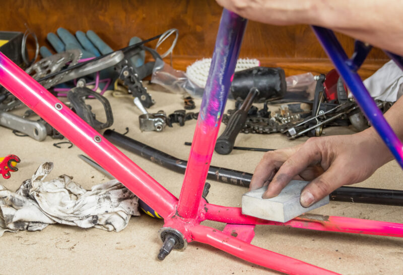 Hands of real bicycle mechanic sanding damaged frame bike in a workshop